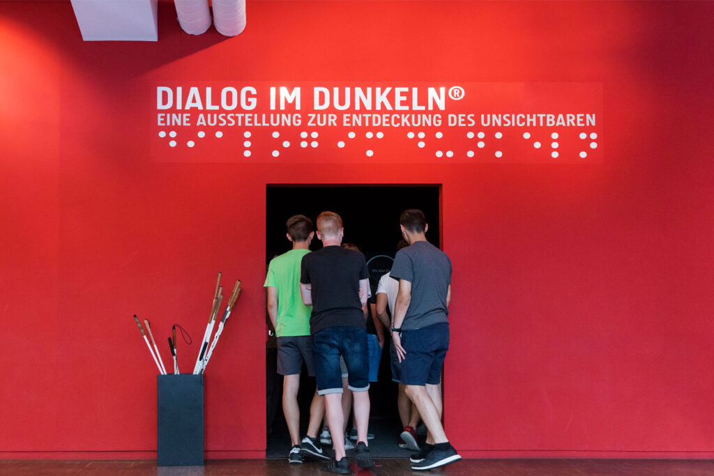 Gruppe betritt Eingang in die Ausstellung "Dialog im Dunkeln" mit einer Gruppe Besucher*innen